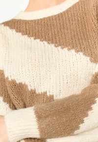 Pleteni pulover z vzorcem rjavih in kremastih cikcak črt, z teksturirano tkanino in rebrastimi manšetami.