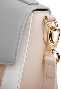 Stylish bag featuring a grey flap, soft beige body, white stripe, and a gold hardware clasp with a smooth texture and elegant stitching.