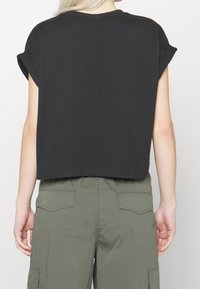 Person wearing a black cropped t-shirt with rolled sleeves and olive green cargo pants, shown from the back against a plain background.