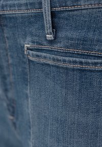Gros plan sur un jean en denim bleu montrant la poche arrière, la passants de ceinture et les coutures détaillées.