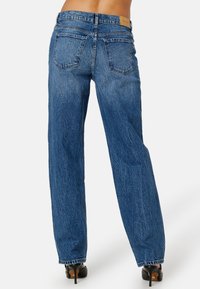 Lösa blå denimjeans med synlig sömnad, två bakfickor och en läderlabel vid midjan. Texturerad, urblekt tyg.