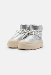 Zapatillas altas plateadas de tipo puffy con cordones blancos y una gruesa suela de goma beige. Presentan una superficie suave y reflectante y punta redondeada.