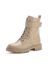 Bottine à lacets beige en matériau synthétique brillant. Elle présente une sangle autour de la cheville, une semelle robuste et des accents de couture contrastants.