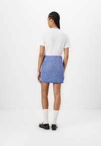 Short-sleeve white t-shirt paired with a blue patterned mini skirt. The skirt features a textured design and is complemented by black shoes.