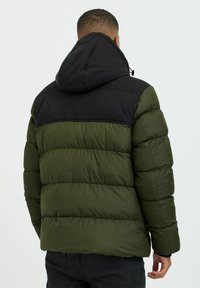 Giacca imbottita con cappuccio nero e parte superiore, caratterizzata da pannelli inferiori verdi, una forma squadrata e una texture liscia con cuciture visibili.
