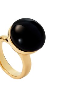 Bague en or avec une large pierre noire ronde lisse mise en valeur sur le dessus, sur un fond blanc.