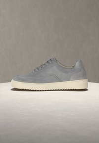 Baskets basses en daim gris clair avec semelle en caoutchouc blanche et lacets, présentées de profil sur un fond neutre.