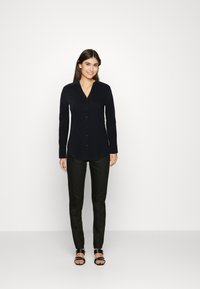 Zwarte lange mouwen shirt met een kraag en knopen aan de voorkant, gecombineerd met zwarte slim-fit broeken en zwarte sandalen. Effen structuur, aansluitend ontwerp.