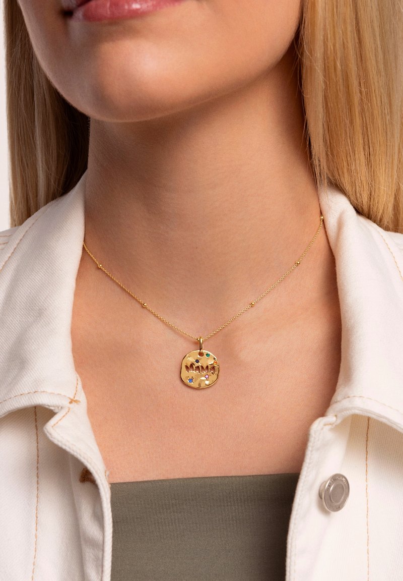Collar con colgante de oro que presenta un charm redondo texturizado con la palabra "MAMA" y pequeñas piedras preciosas de colores. La cadena tiene delicadas cuentas.