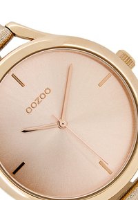 Montre-bracelet en or rose au design minimaliste, dotée d'un cadran métallique lisse, d'indicateurs horaires fins et d'un bracelet texturé.