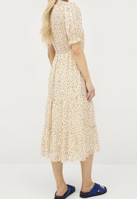 Ljus persikofärgad blommig klänning med korta puffärmar, lagerdesign och ett samlat midja. Bärs med blå glidande sandaler.