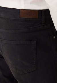 Zwarte katoenen broek met een bruine leren label met daarop "HACKETT." Beschikt over een achterzak en subtiele stiksels, en toont een gladde textuur.