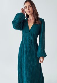 Tyrkysové maxi šaty s krčkováním, dlouhými nadýchanými rukávy, hlubokým výstřihem do V a řadou knoflíků vpředu. Texturovaná tkanina s volným střihem.