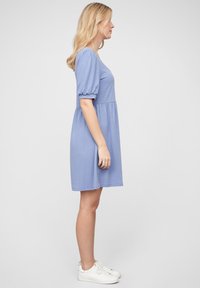 Blå bomullsklänning med korta puffärmar, figurnära bodice och utsvängd kjol. Tillsammans med vita sneakers, texturerad tyg och enkel design.