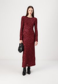 Long burgundy sequin dress with long sleeves, round neckline, and slim fit. Accompanied by a black handbag and heeled ankle boots.