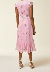 Rosa blommig klänning med korta ärmar, figurnära midja och volangkant, gjord av lätt material med delikata blommönster.