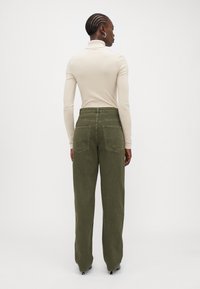Bežs garām piedurknēm turtlenecks, kas saskaņots ar olīvzaļām platām biksēm ar diviem aizmugurējiem kabatām un gludu tekstūru.