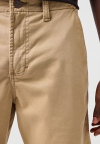 Spodnie bawełniane w kolorze khaki o gładkiej fakturze, prostym kroju i detalach w postaci bocznych kieszeni. Posiadają widoczne szwy oraz zapięcie na guzik.
