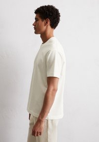 Light beige short-sleeve t-shirt made from soft fabric, featuring a crew neck and relaxed fit. Smooth texture and minimal design details.