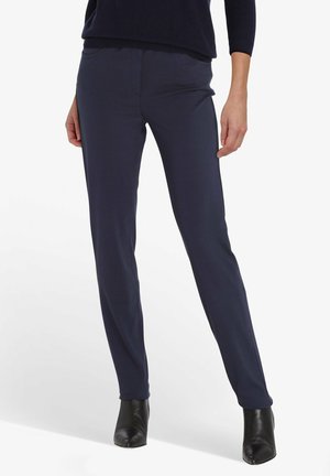 Marineblauwe op maat gemaakte broek met een slank ontwerp, aangesloten snit en subtiele voorzakken. Gepaard met zwarte spitse enkellaarzen.