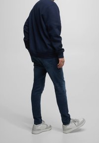 Sudadera de color navy con puños acanalados, combinada con jeans oscuros ajustados y zapatillas grises con detalles blancos, vista de lado.