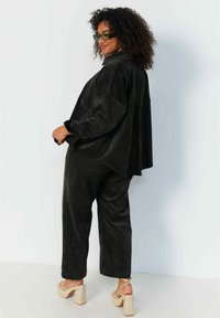 Zwarte velours wijde broek gecombineerd met een bijpassend oversized shirt. Opvallende kenmerken zijn de zachte textuur en de relaxte snit.