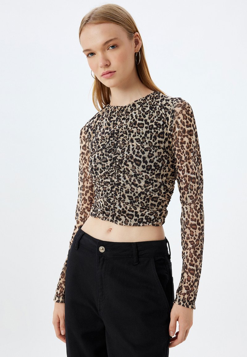 Top a maniche lunghe con stampa leopardata, dettaglio arricciato sul davanti, tessuto trasparente, scollatura rotonda e design accorciato abbinato a pantaloni neri a vita alta.