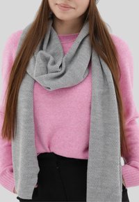 Sciarpa grigia lavorata a maglia avvolta attorno al collo, con un motivo testurizzato. Indossata con un maglione rosa, creando un contrasto di colori.