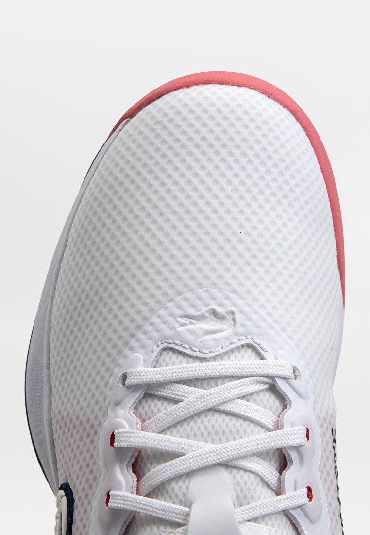 Zapatilla deportiva blanca con parte superior de malla texturizada, acentos rojos en el cuello y cordones blancos sobre ojales reforzados. Presenta detalle del logo.