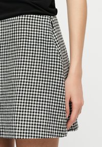 Μαύρη και άσπρη φούστα με καρό σχέδιο, φορεμένη με μαύρο τοπ, εμφανίζοντας τη δεξιά πλευρά της φούστας και ένα μερικώς ορατό βραχίονα.