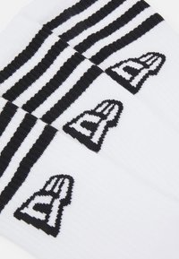 Calcetines de crew blancos con rayas horizontales negras. Cada calcetín tiene un gráfico del logotipo negro cerca del tobillo. Textura suave y acanalada.