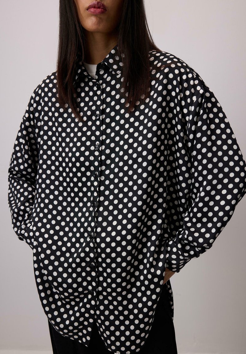 Czarna i biała koszula w grochy wykonana z gładkiej tkaniny, z zapięciem na guziki z przodu, oversize'owym krojem i opadającymi ramionami.
