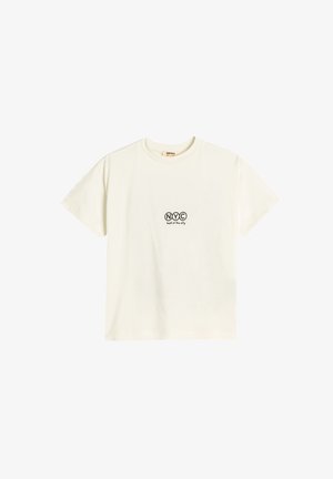 Cremefarvet bomulds T-shirt med korte ærmer, prydet med sort print "NYC" og teksten "bedst i byen" nedenfor. Rund hals, blød tekstur.