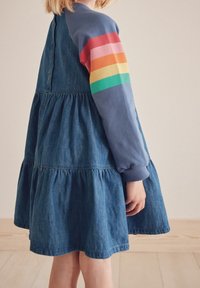 Abito di jeans con design a strati, in tessuto blu, e maniche lunghe caratterizzate da strisce orizzontali colorate in rosso, arancione, giallo, verde e blu.