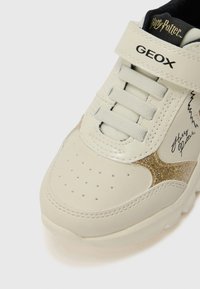Witte leren sneaker met gouden glitteraccenten, gestructureerde neus, geventileerde zijkanten, veters en klittenbandsluiting, met een Harry Potter ontwerp.