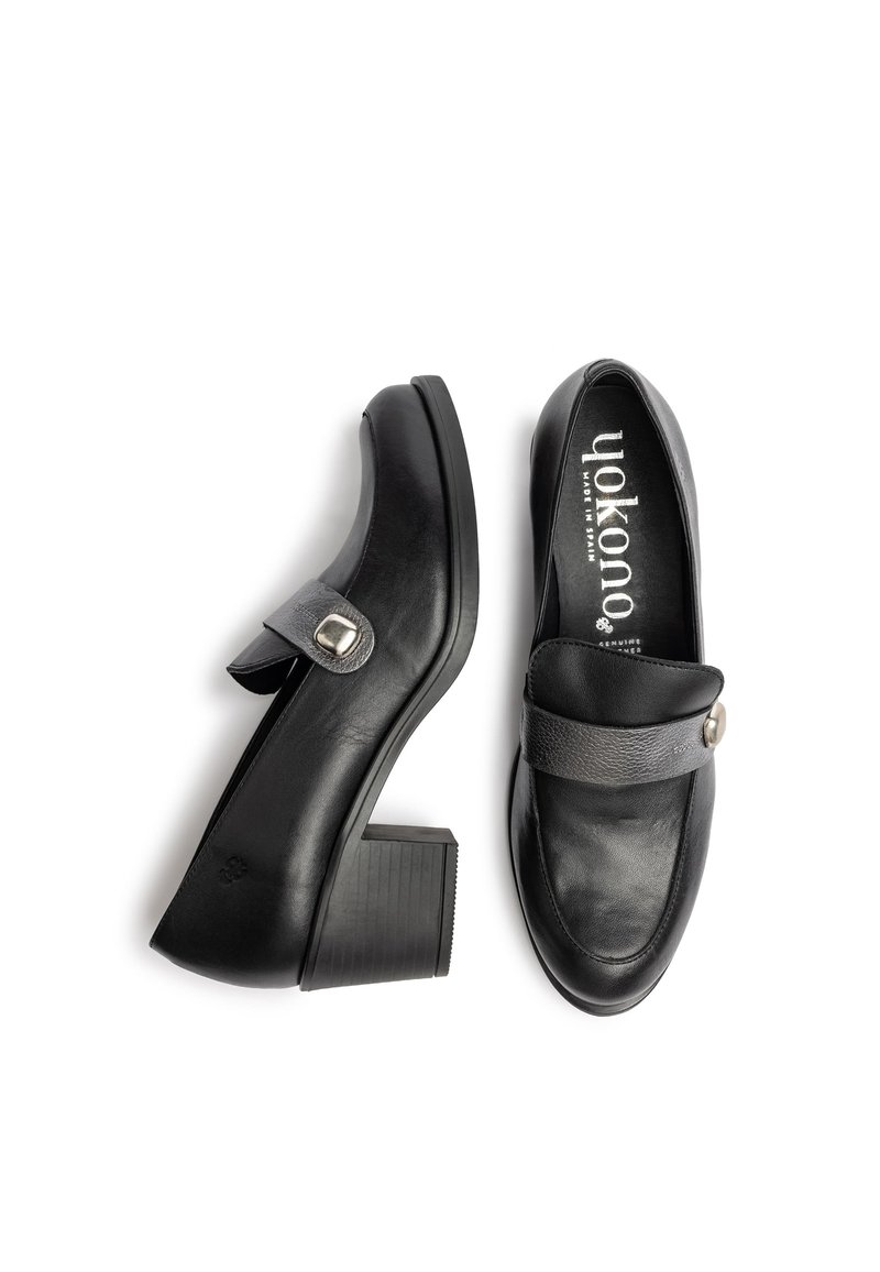 Mocasines de tacón de cuero negro con punta redonda, una correa ancha en el empeine y un detalle de hebilla metálica circular. Tacón de bloque texturizado.
