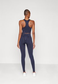 Mørk marine sports-bh med racerback-design, kombinert med matchende leggings med høy midje. Glatt, stretchy stoff.