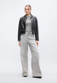 Μαύρο cropped δερμάτινο μπουφάν πάνω από ριγέ μακρυμάνικη μπλούζα, συνδυασμένο με φαρδιά ανοιχτόγκρι τζιν και μαύρες μποτάκια αστραγάλου.