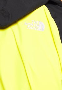 Giacca gialla e nera realizzata in tessuto leggero, con un design elegante e il logo ricamato "The North Face" sul petto.