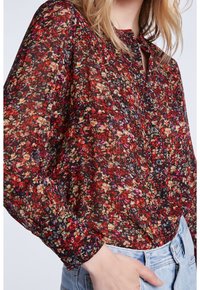 Blouse à manches longues en imprimé floral sombre, dotée d'un col en keyhole, d'une fermeture à bouton et d'une texture de tissu léger et transparent.