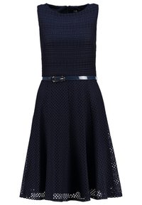 Robe sans manches bleu marine avec corsage texturé, jupe évasée et ceinture brillante. Motif œillet sur l'ensemble du tissu.