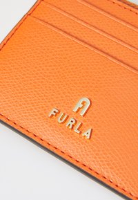 Kollane nahast kaarditasku, millel on mitu kaardipesa, tekstureeritud pinnaga ning kuldne logo "FURLA", mis on silmatorkavalt esitatud.
