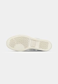 Shoe sole with a textured white rubber surface, featuring a geometric pattern and brand logo, rounded shape, and slightly raised edges.