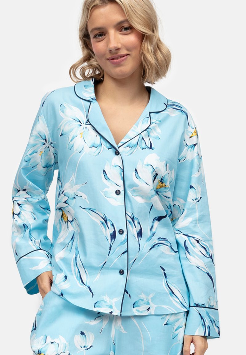Conjunto de pijama floral en azul claro que incluye una camisa de botones con ribetes negros y mangas largas, combinada con pantalones a juego.