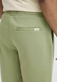 Lys grønne sweatpants med elastisk talje, der har en baglomme og et lille mærke. Blødt, textured stof med en afslappet pasform.