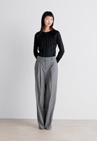 Musta pitkähihainen paita, jossa on kerrostettu kaula-aukko, yhdistettynä korkeavyötäröisiin harmaisiin raidallisiin housuihin, joissa on taitteita ja sivunapit.