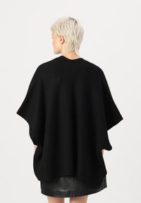 Svart stickad poncho i ribbat material med avslappnad passform, vida ärmar och en rundad fåll nertill.