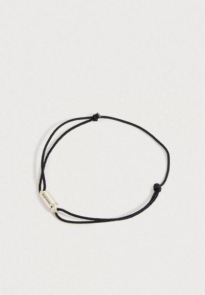 Podesiva crna narukvica na konopcu s malim srebrnim pravokutnim perlicom ugraviranom s "le gramme" i drugim oznakama.