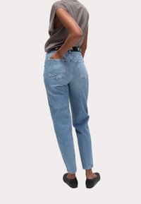 Světle modré džíny s vysokým pasem a uvolněným střihem, vybavené zadními kapsami a tmavým páskem. Tkanina vypadá jako denim s jemnou texturou.