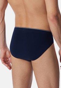 Culotte en coton bleu marine au design uni, avec une ceinture contrastante dotée d'une fine ligne blanche. Présentée de dos, mettant en avant l'ajustement.